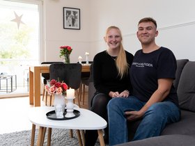 Ein Mieterpaar sitzt im heimischen Wohnzimmer auf der Couch. Beide lächeln und schauen in die Kamera.